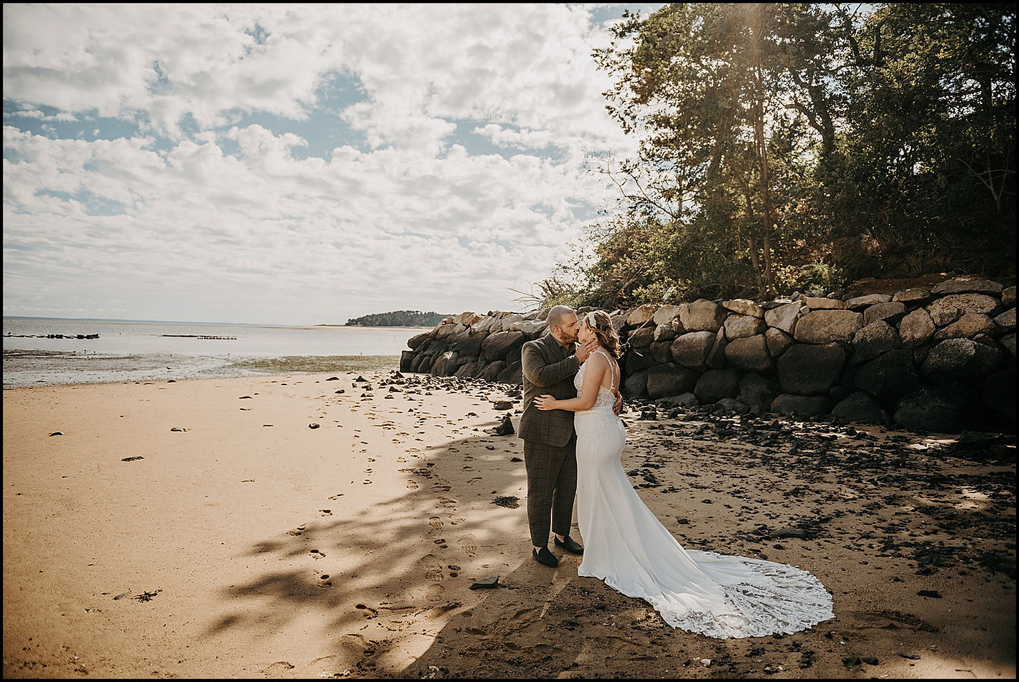 A bride and groom kiss in a patch of shade on the beach outside the Chequessett Club.
