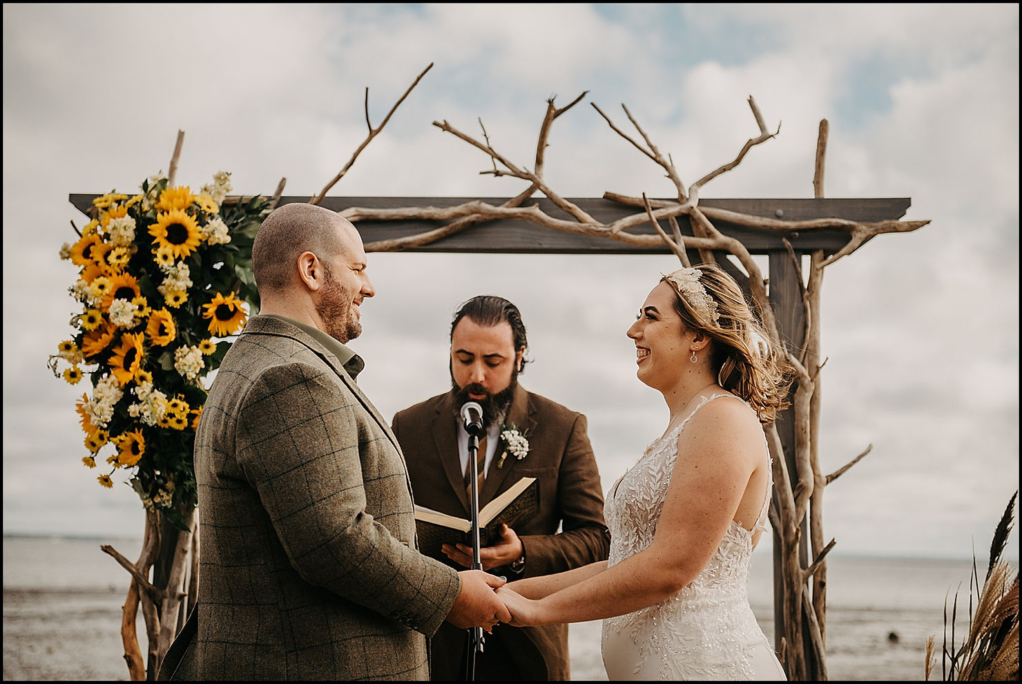 A bride and groom hold hands on a windy beach during a ceremony at a Cape Cod wedding venue.