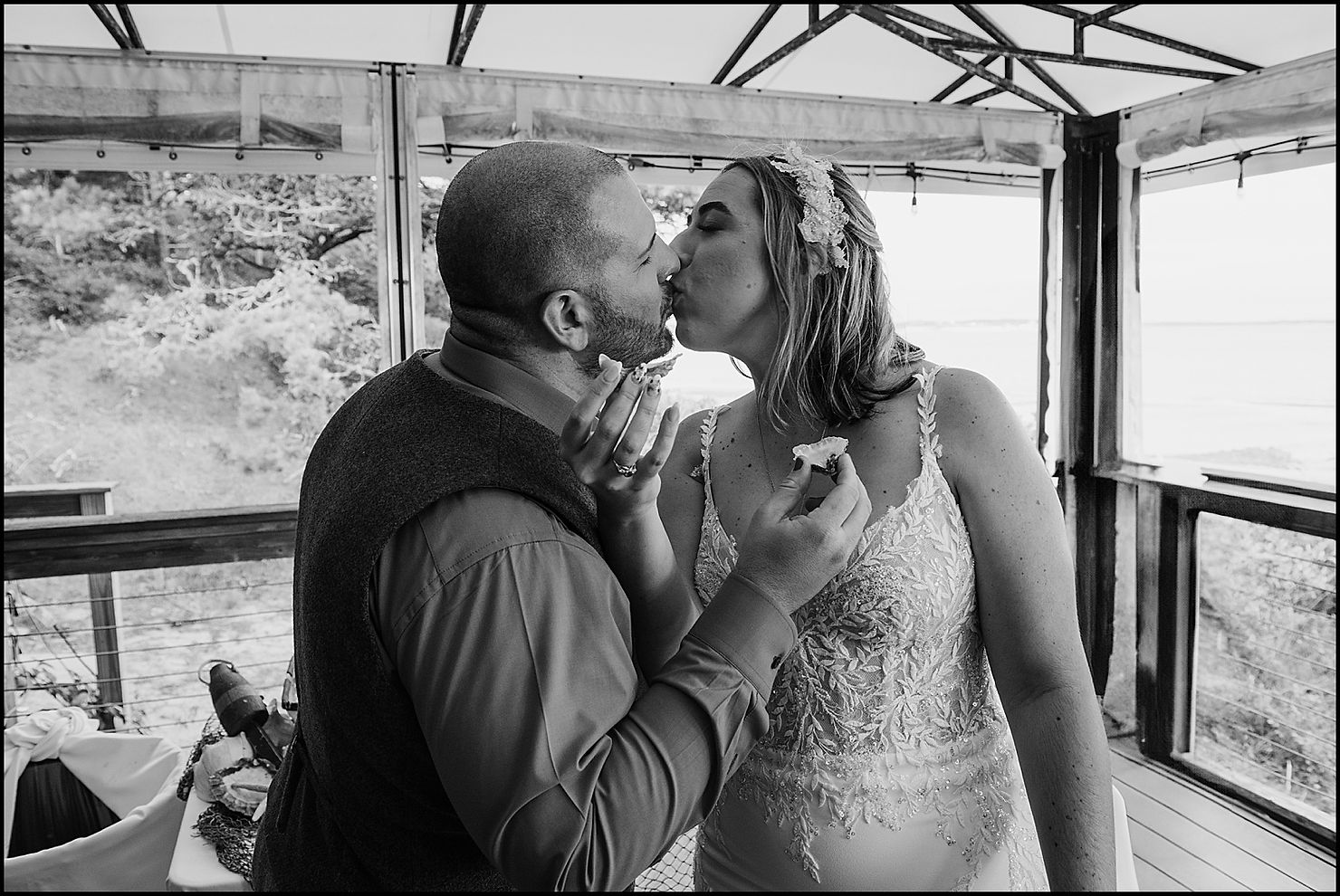 A bride and groom kiss on a covered deck.
