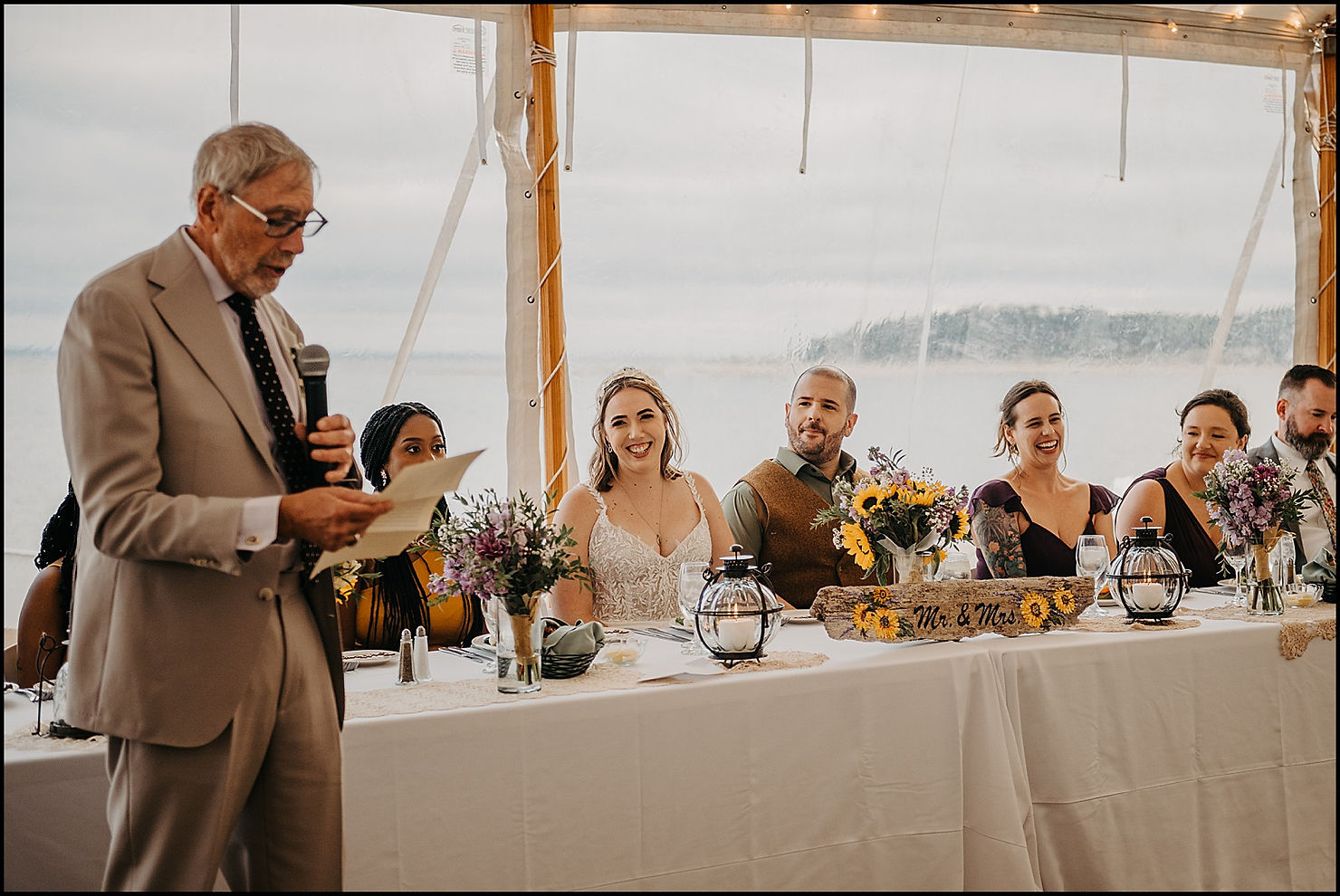 A bride laughs at the head table while a family member gives a speech at a Chequessett Club wedding.