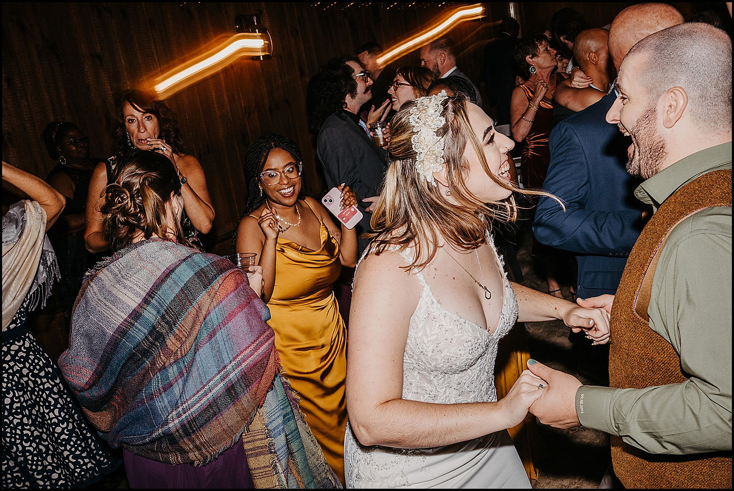 A bride and groom dance smiling on a crowded dance floor.