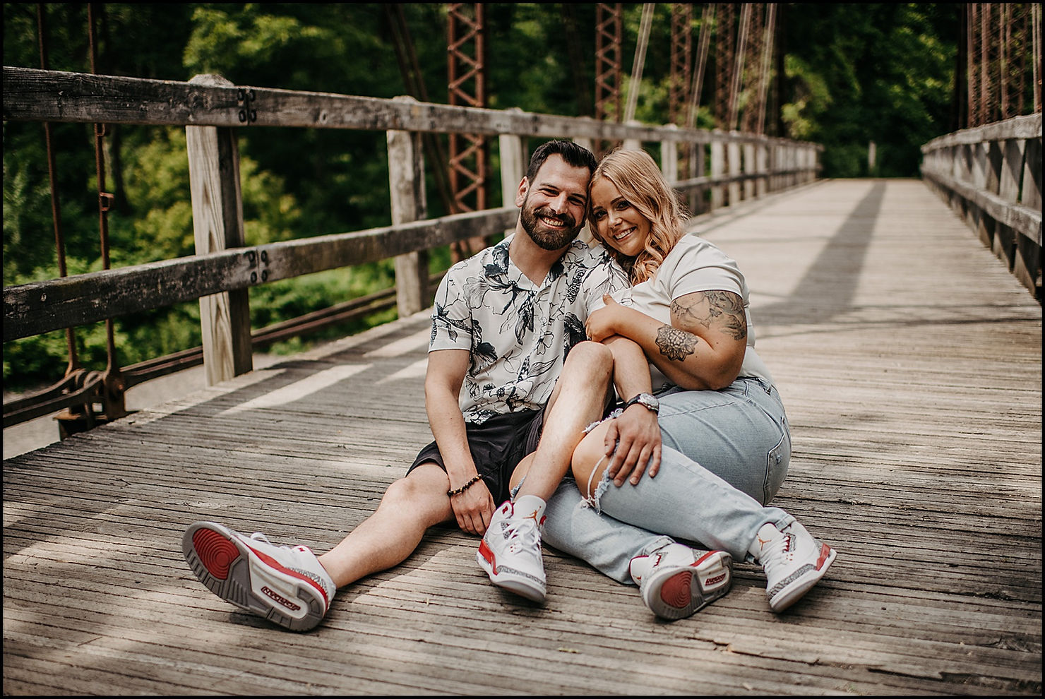 An engaged man and woman sit next to each other on a bridge at Eighteen Mile Creek.