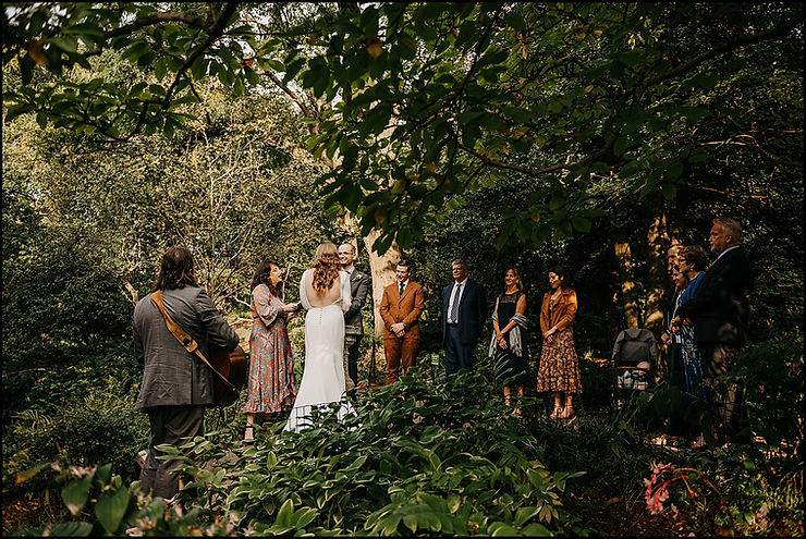 Family members stand in the shade of a tree to watch a wedding ceremony in Shakespeare Garden Central Park.