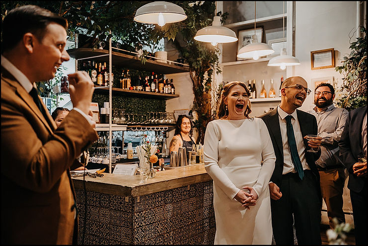 A bride and groom laugh during a best man's speech at a restaurant wedding reception.
