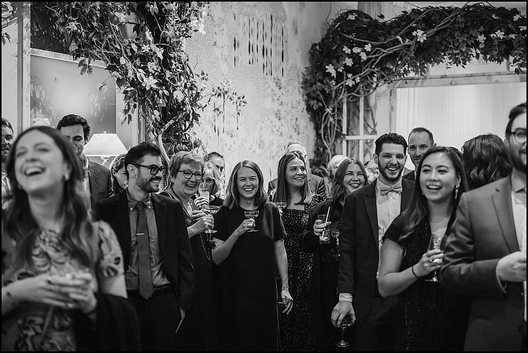 Wedding guests laugh in a New York restaurant decorated with flowering trees.