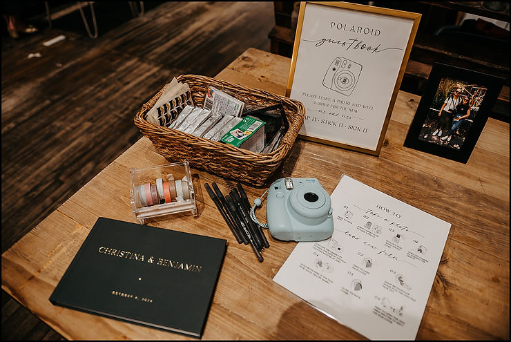 An instax camera sits beside a guest book at a wedding welcome table.